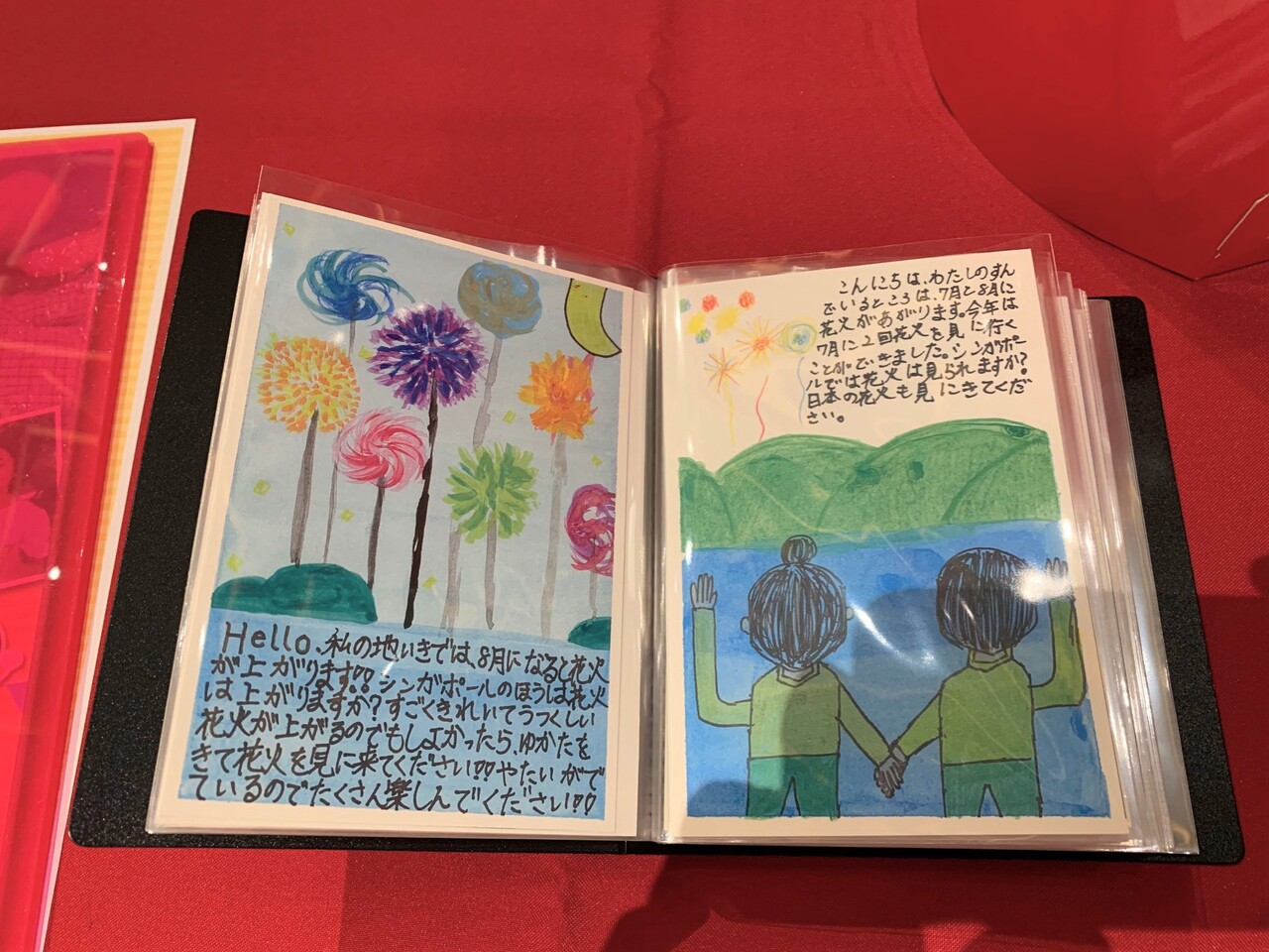 左側にカラフルな花火の絵と花火を説明した文章が添えられた絵手紙、右には手を繋いだ人が花火を見ている絵が描かれ花火を説明した文章が添えられた絵手紙の写真