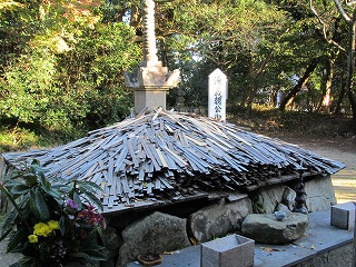 大きな石の上にに沢山の木太刀が奉納されている源義朝公の墓を斜め正面から写した写真