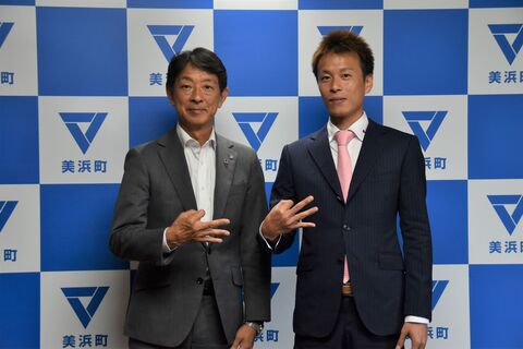 美浜町のバックボードの前で、磯部選手と町長が手でサインを作って同じポーズで撮っている写真