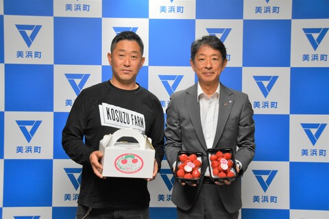 美浜町のバックボードの前で、小鈴ファームの方と町長が金賞を受賞したトマトを持っている写真