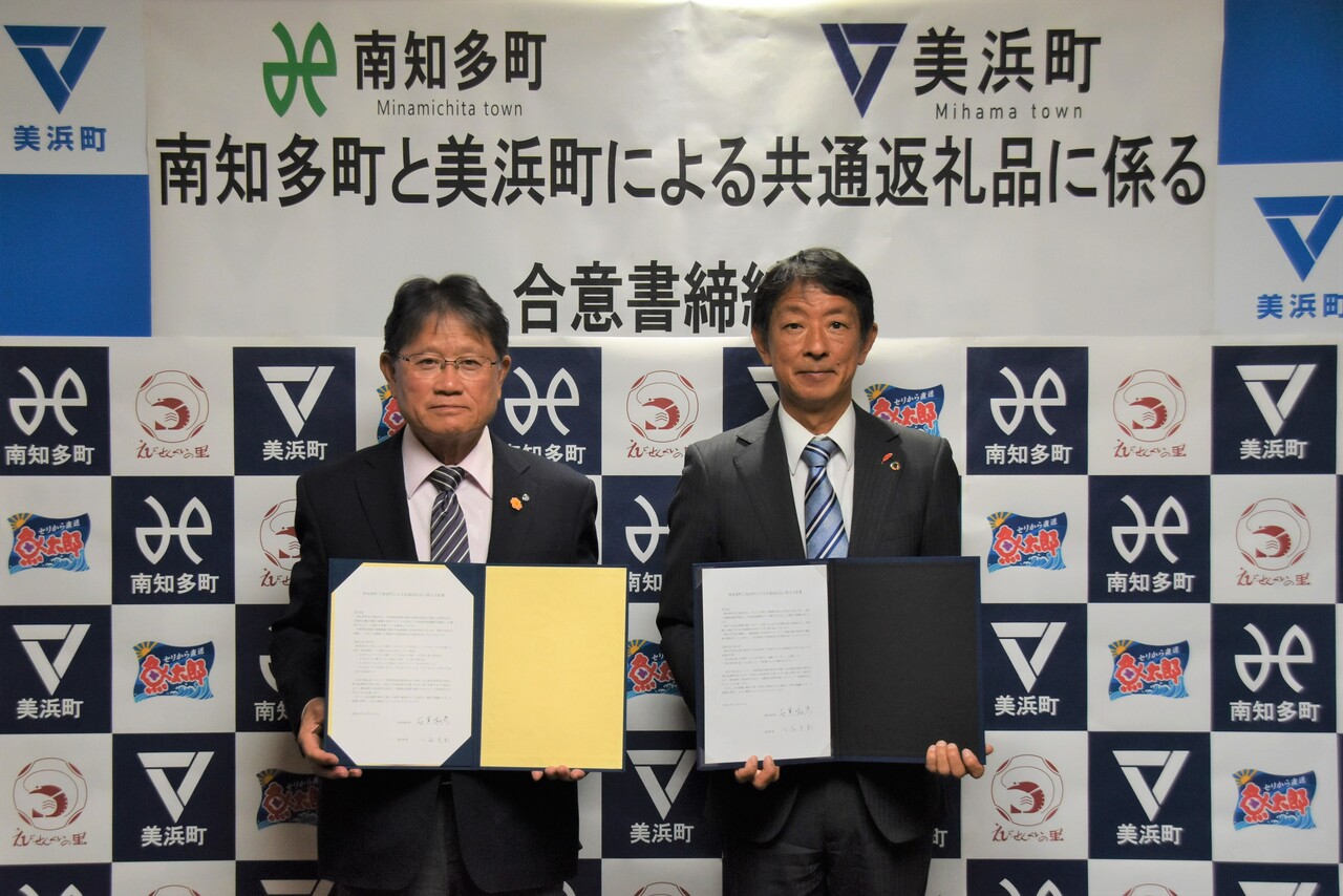 美浜町・南知多町・魚太郎株式会社様・株式会社えびせんべいの里ホールディングス様のバックボードの前で、美浜町と南知多町の町長が合意書を持ち記念撮影をしている写真