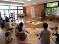 前で女性が話をしており、たくさんの親子連れの参加者が座ってお話を聞いている子育て支援センターの様子を写した写真