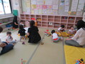 畳の部屋で絵本の並んだ本棚、女性職員に見守られながら、玩具で遊んでいる乳幼児と親子が写っている親子交流スペースでの写真