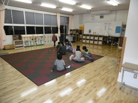 フローリングの床になっている広い室内にチェック柄のカーペットが敷かれ、その上で児童たちが遊んでいる様子の奥田児童クラブ室内の写真