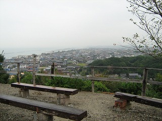 高台で町が見渡せる場所にベンチが設置され、木のフェンスの向こうに美浜町の町並みが広がる冨具崎公園の絶景写真