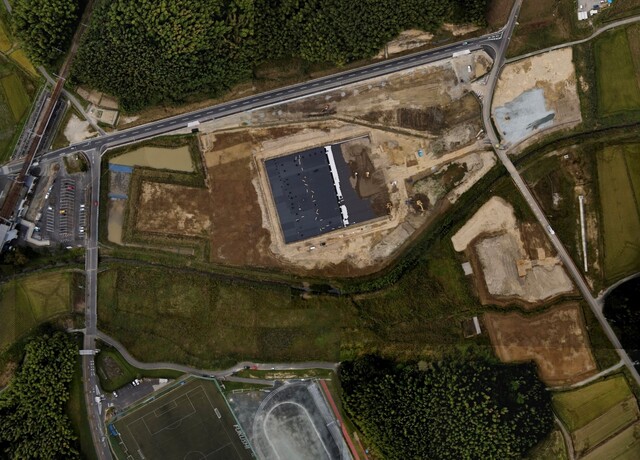 周囲を鬱蒼と茂った森が点在する建設予定地で調整池の設置工事が行われている様子を令和3年(2021)年10月上空から撮影した写真