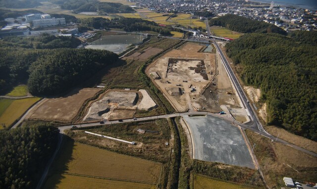 周囲に民家や鬱蒼と茂った森が点在する陸上競技場の建設予定地で、調整池の設置工事が進められている様子を令和3年(2021)年11月斜め上空から撮影した写真