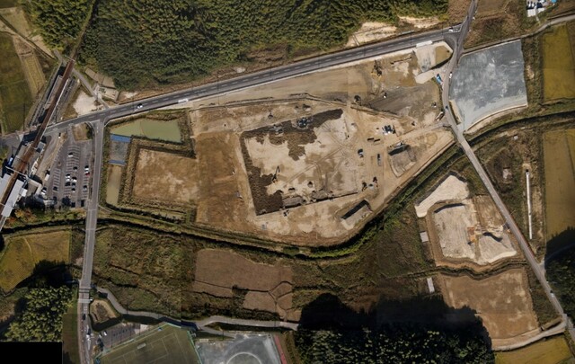 周囲を鬱蒼と茂った森が点在する建設予定地で調整池の設置工事が行われている様子を令和3年(2021)年11月上空から撮影した写真