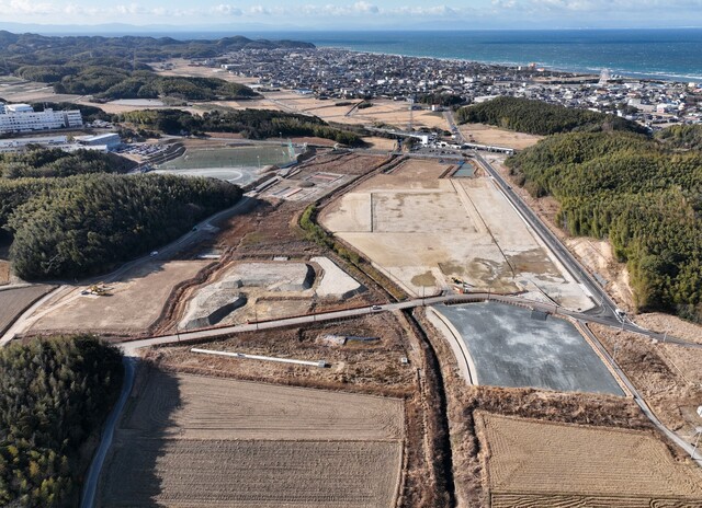 周囲に民家や鬱蒼と茂った森が点在する陸上競技場の建設予定地で、観覧スタンドの基盤設備工事が進められている様子を令和4年(2022)年1月斜め上空から撮影した写真