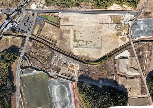 周囲を鬱蒼と茂った森が点在する建設予定地で、観覧スタンドの基盤設備工事が行われている様子を令和4年(2022)年1月上空から撮影した写真