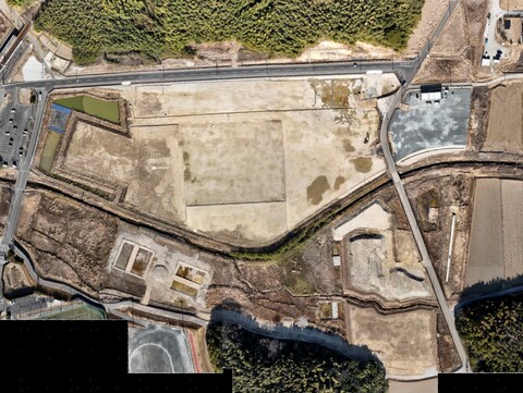 周囲を鬱蒼と茂った森が点在する建設予定地で、観覧スタンドの基盤設備工事が行われている様子を令和4年(2022)年2月上空から撮影した写真