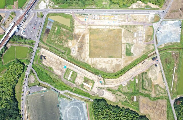 周囲を鬱蒼と茂った森が点在する建設予定地で、観覧スタンドと器具庫の工事が進められている様子を令和4年(2022)年7月上空から撮影した写真