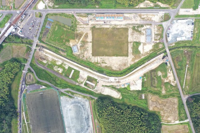 周囲を鬱蒼と茂った森が点在する建設予定地で、観覧スタンドと器具庫の工事が行われている様子を令和4年(2022)年9月上空から撮影した写真