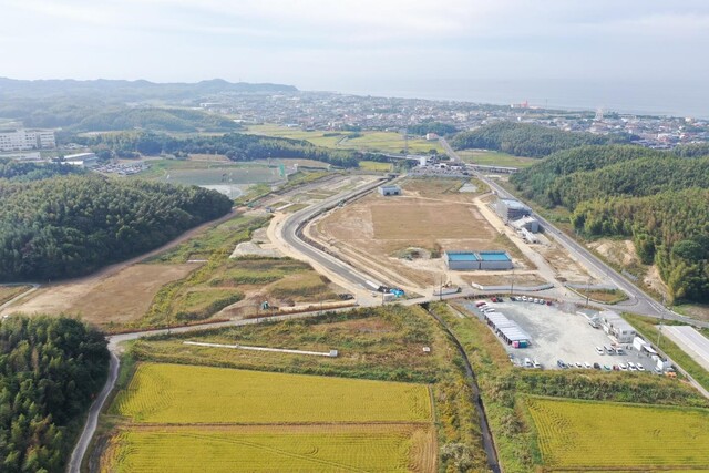 周囲に民家や鬱蒼と茂った森が点在する陸上競技場の建設予定地で工事が進められている様子を令和4年(2022)年10月斜め上空から撮影した写真