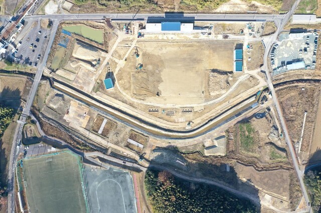 周囲を鬱蒼と茂った森が点在する建設予定地で工事が行われている様子を令和4年(2022)年12月上空から撮影した写真