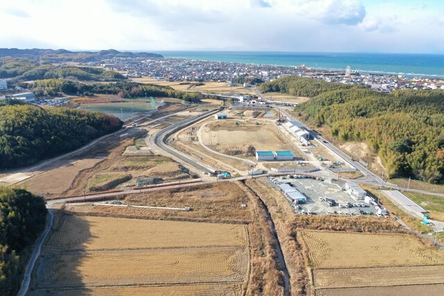 周囲に民家や鬱蒼と茂った森が点在する陸上競技場の建設予定地で工事が進められている様子を令和4年(2022)年12月斜め上空から撮影した写真