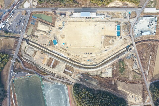 周囲を鬱蒼と茂った森が点在する建設予定地で工事が行われている様子を令和5年(2023)年1月上空から撮影した写真