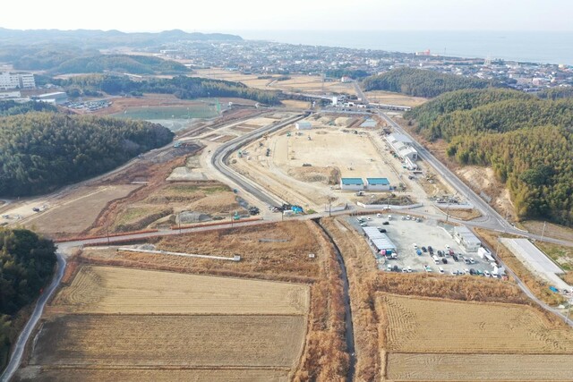 周囲に民家や鬱蒼と茂った森が点在する陸上競技場の建設予定地で工事が進められている様子を令和5年(2023)年1月斜め上空から撮影した写真