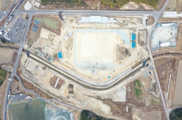 周囲を鬱蒼と茂った森が点在する建設予定地で工事が行われている様子を令和5年(2023)年2月上空から撮影した写真