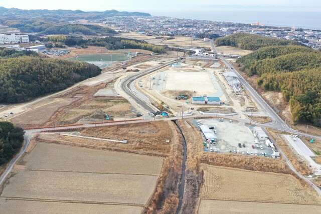 周囲に民家や鬱蒼と茂った森が点在する陸上競技場の建設予定地で工事が進められている様子を令和5年(2023)年2月斜め上空から撮影した写真