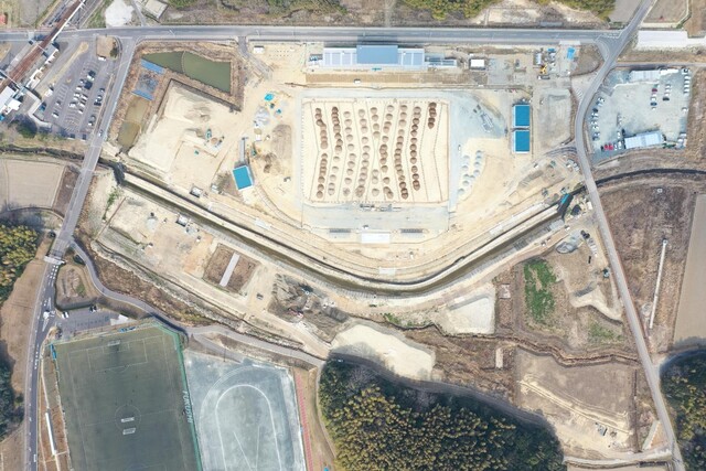 周囲を鬱蒼と茂った森が点在する建設予定地で工事が行われている様子を令和5年(2023)年3月上空から撮影した写真