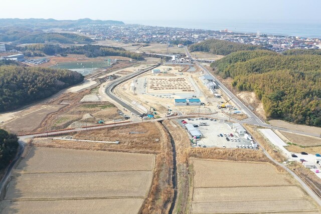 周囲に民家や鬱蒼と茂った森が点在する陸上競技場の建設予定地で工事が進められている様子を令和5年(2023)年3月斜め上空から撮影した写真