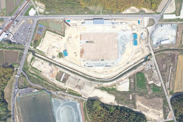 周囲を鬱蒼と茂った森が点在する建設予定地で工事が行われている様子を令和5年(2023)年4月上空から撮影した写真