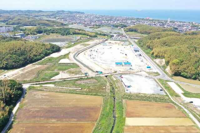 周囲に民家や鬱蒼と茂った森が点在する陸上競技場の建設予定地で工事が進められている様子を令和5年(2023)年5月斜め上空から撮影した写真