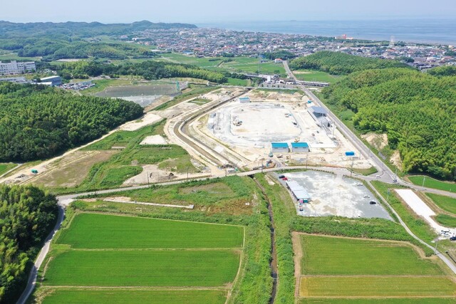 周囲に民家や鬱蒼と茂った森が点在する陸上競技場の建設予定地で工事が進められている様子を令和5年(2023)年6月斜め上空から撮影した写真