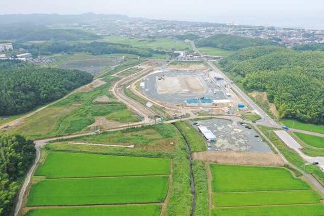 周囲に民家や鬱蒼と茂った森が点在する陸上競技場の建設予定地で工事が進められている様子を令和5年(2023)年7月斜め上空から撮影した写真