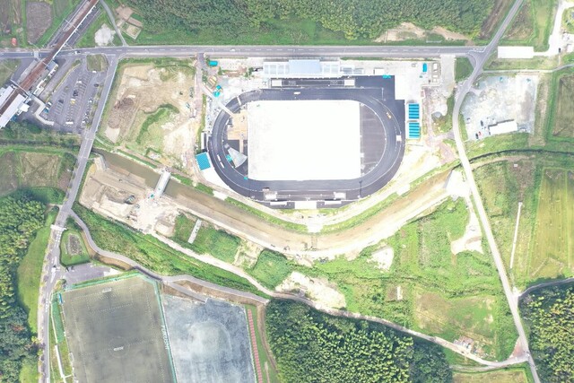 周囲を鬱蒼と茂った森が点在する建設予定地で工事が行われている様子を令和5年(2023)年9月上空から撮影した写真