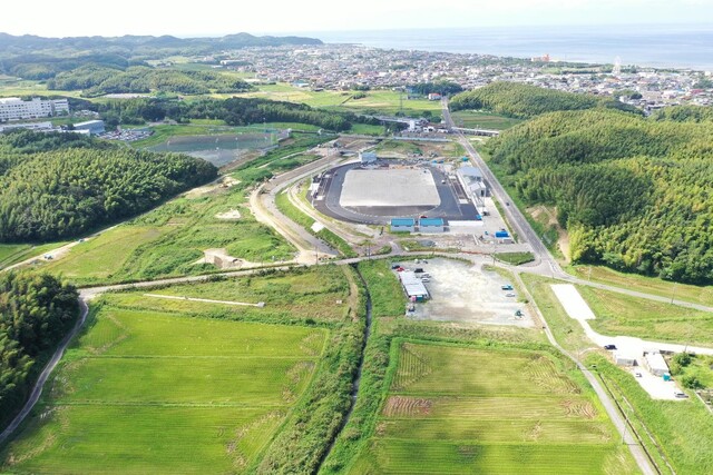 周囲に民家や鬱蒼と茂った森が点在する陸上競技場の建設予定地で工事が進められている様子を令和5年(2023)年9月斜め上空から撮影した写真