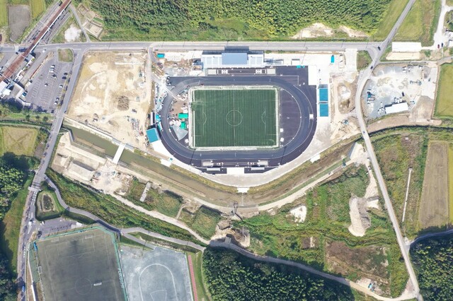 周囲を鬱蒼と茂った森が点在する建設予定地で工事が行われている様子を令和5年(2023)年10月上空から撮影した写真