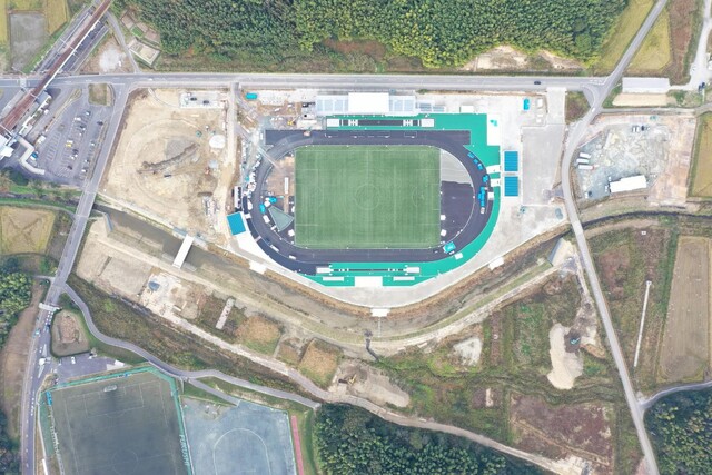 周囲を鬱蒼と茂った森が点在する建設予定地で工事が行われている様子を令和5年(2023)年11月上空から撮影した写真