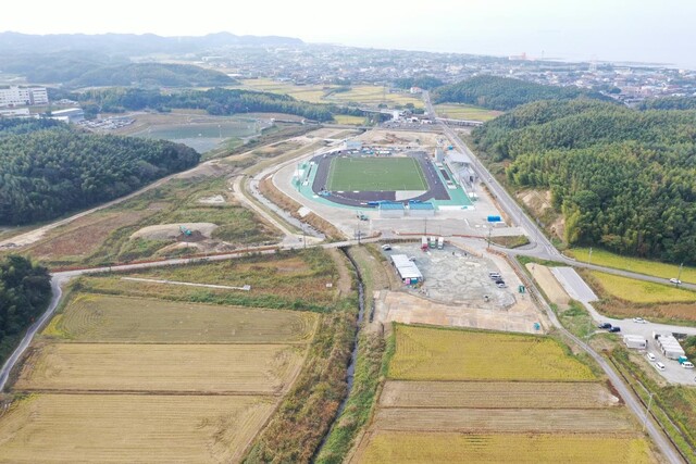 周囲に民家や鬱蒼と茂った森が点在する陸上競技場の建設予定地で工事が進められている様子を令和5年(2023)年11月斜め上空から撮影した写真