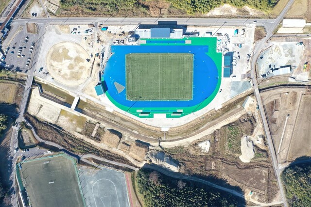 周囲を鬱蒼と茂った森が点在する建設予定地で工事が行われている様子を令和5年(2023)年12月上空から撮影した写真