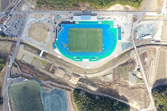 周囲を鬱蒼と茂った森が点在する建設予定地で工事が行われている様子を令和6年(2024)年1月上空から撮影した写真