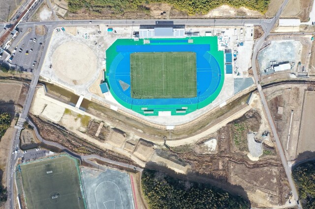 周囲を鬱蒼と茂った森が点在する建設予定地で工事が行われている様子を令和6(2024)年2月上空から撮影した写真