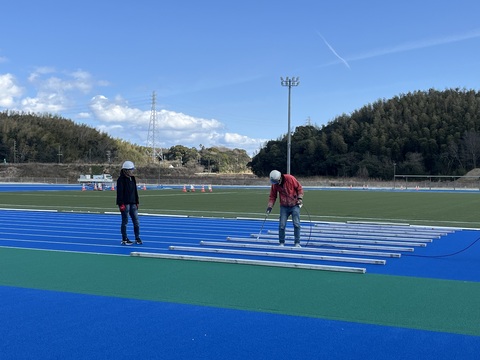 ヘルメットを被り防寒着を着用した2名の作業員が、直線のトラック部分のラインマーキング工事を行っている様子の写真