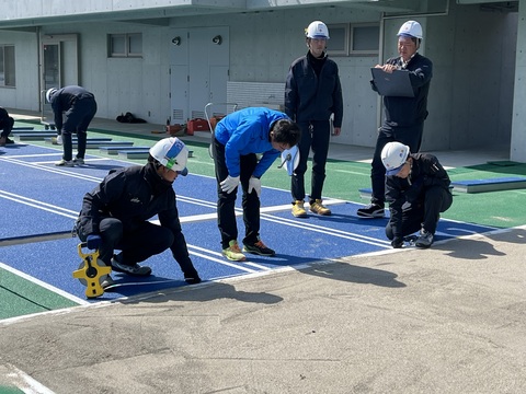 ヘルメットを被った作業員がメジャーで長さの確認を行い、後ろでヘルメット被った作業員がメモを取っている様子の写真