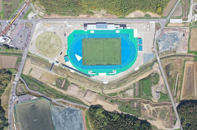 周囲を鬱蒼と茂った森が点在する建設予定地で工事が行われている様子を令和6(2024)年4月上空から撮影した 全景写真