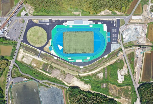 周囲を鬱蒼と茂った森が点在する建設予定地で工事が行われている様子を令和6(2024)年5月上空から撮影した写真