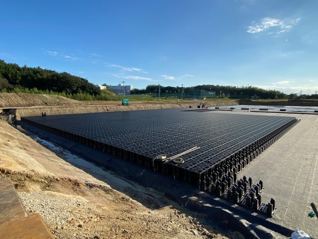 黒色のプラスチック製の資材が組み立てられ、陸上競技場予定地の地下に設置される調整池の設置工事を行っている様子の写真