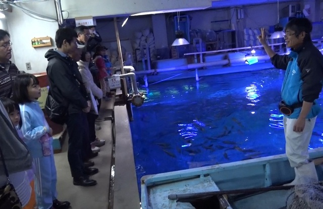 魚が入っている大水槽の上側に参加者たちが集まり、飼育員の方の説明を聞いている様子の写真