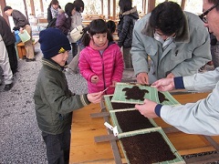 男性が持っている巻きすの上に置かれた亀の形をした海苔を見ている男の子と女の子の写真