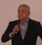 スーツ姿の鈴木教授が右手でマイクを持って話をしている写真