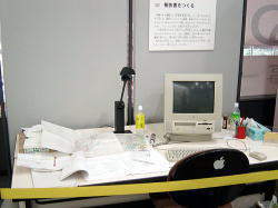 机上にパソコンや資料が置かれている報告書作成の様子を再現した展示室の写真