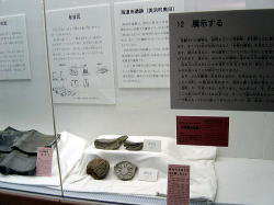ショーケース内の白い布の上に土器が置かれ、遺物や展示方法の解説などが書かれたプレートが展示されている写真