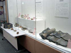 白い布の上に土器が置かれ、遺物や展示方法の解説などが書かれたプレートが展示されているショーケース内を向かって右側から写した写真