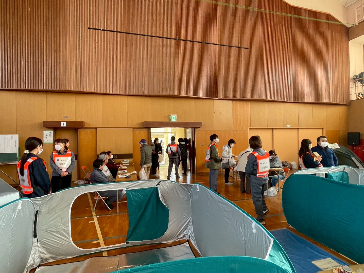 南部体育館入り口に設置された受付で、受付をする地元区住民。写真手前ではパーテーションで仕切られた避難所が再現されている。